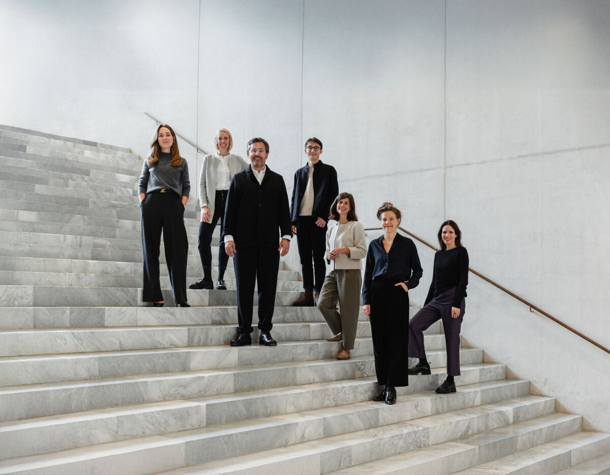 Das FUTUN-Kollektiv steht auf Treppenstufen in einem Treppenhaus aus Marmor und Beton