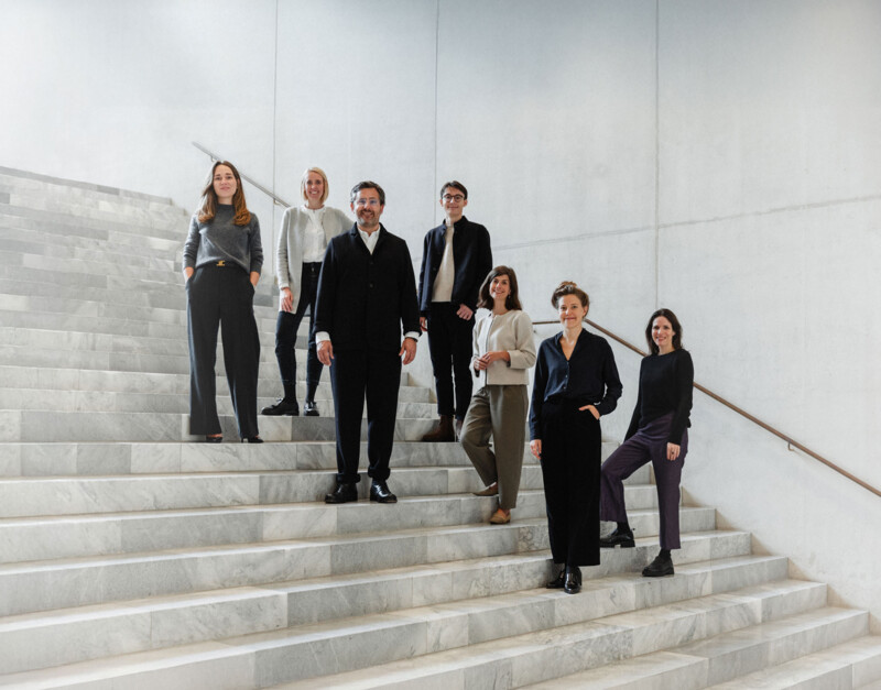 Das FUTUN-Kollektiv steht auf Treppenstufen in einem Treppenhaus aus Marmor und Beton