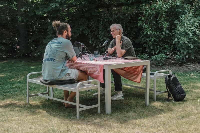 Oskar Trautmann und Michael Trautmann sitzen auf B&auml;nken an einem Tisch in einem Garten. Sie sitzen sich gegen&uuml;ber und sprechen miteinander. Auf dem Tisch stehen Mikrofone und ein Aufnahmeger&auml;t.