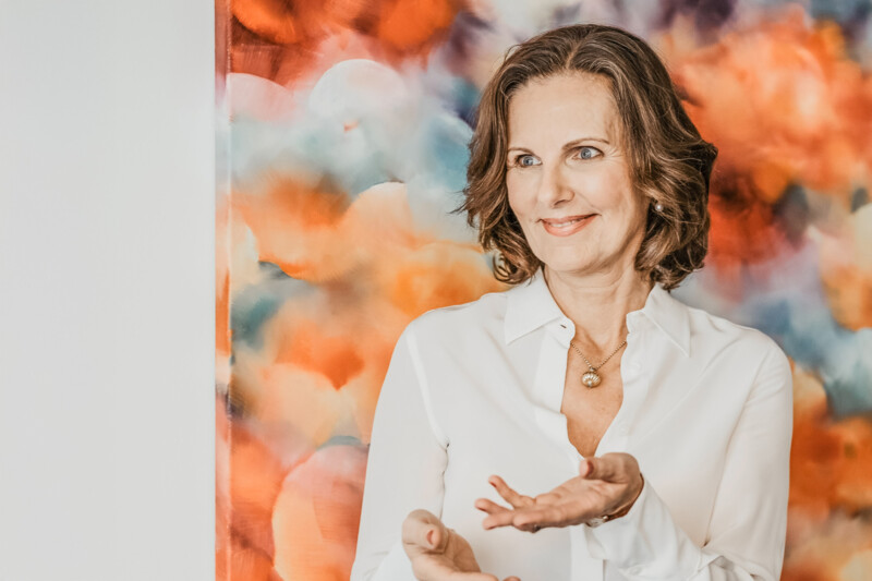 Petra Becker steht vor einem bunten abstrakten Gemälde