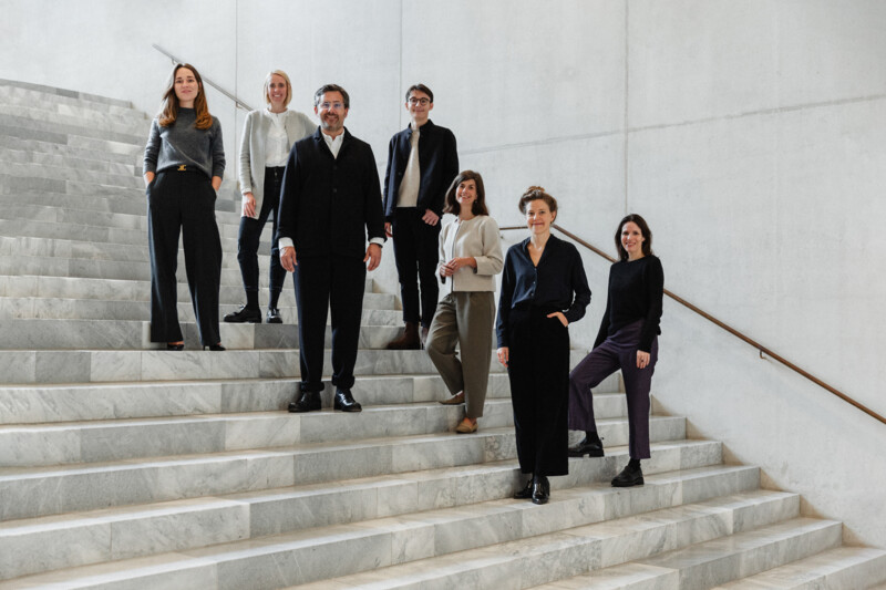 Das FUTUN-Kollektiv steht auf Treppenstufen in einem Treppenhaus aus Marmor und Beton